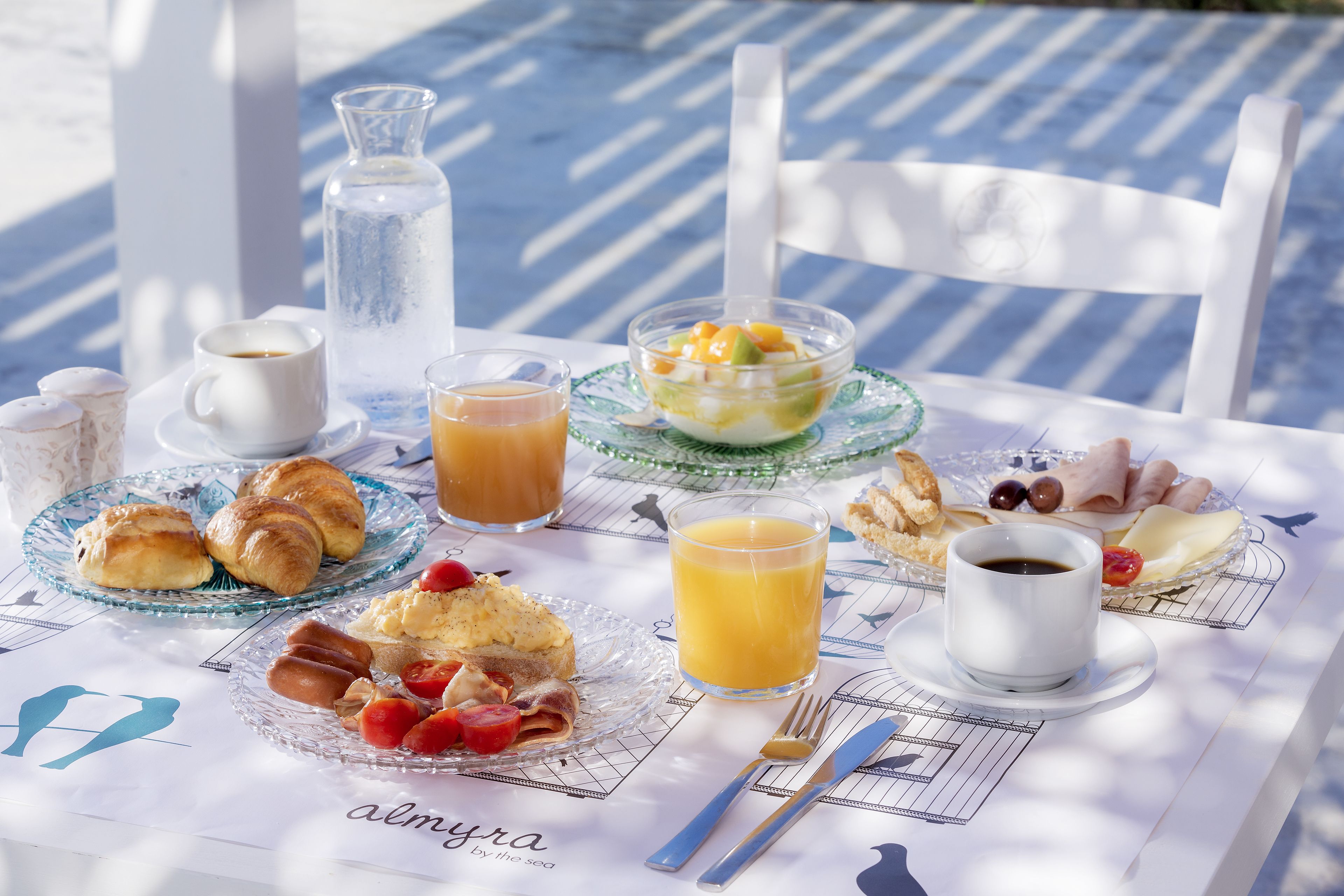 A breakfast table with croissants, fruit, coffee, and juice.