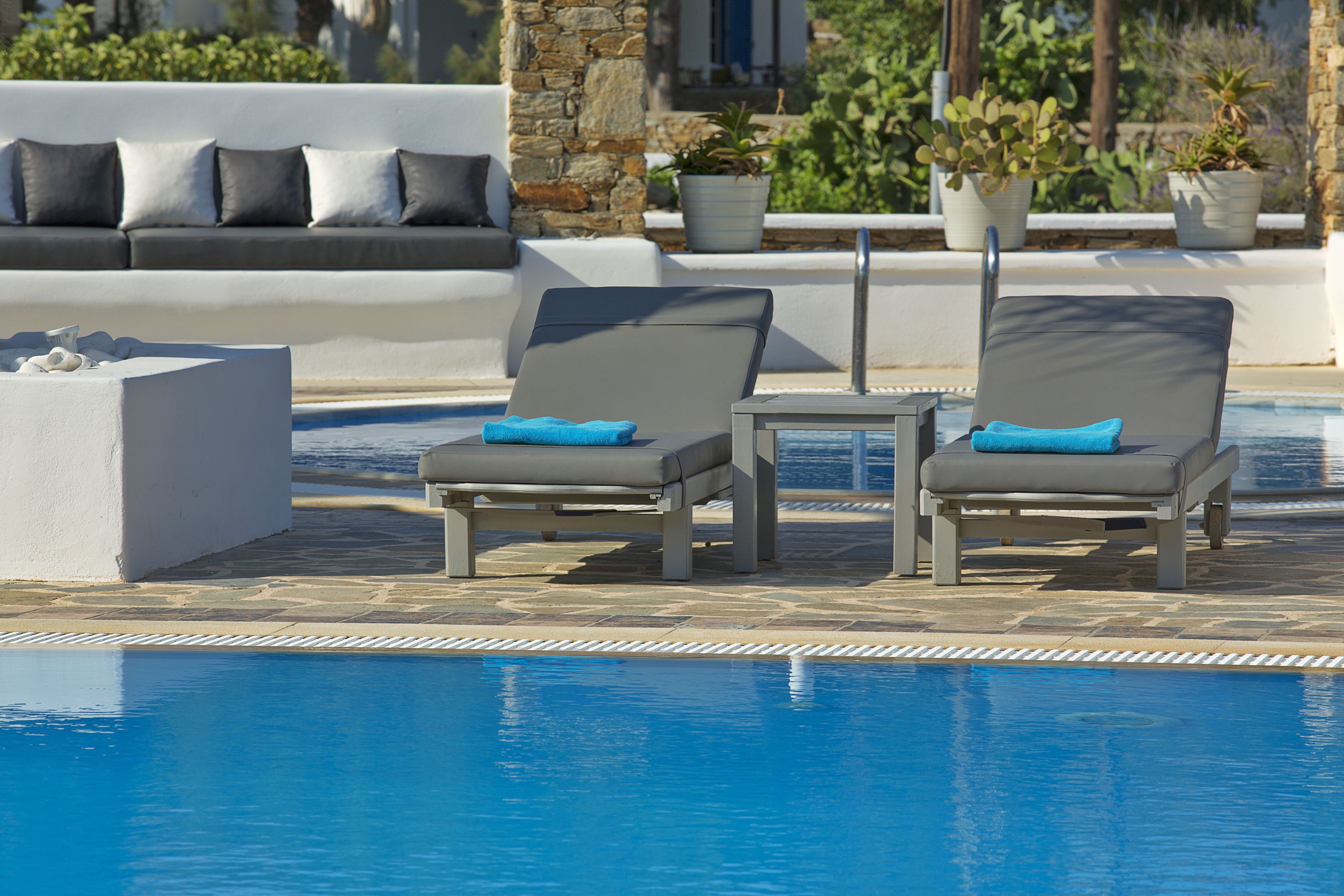 A poolside area with two lounge chairs, a small table, and a white sofa with cushions.
