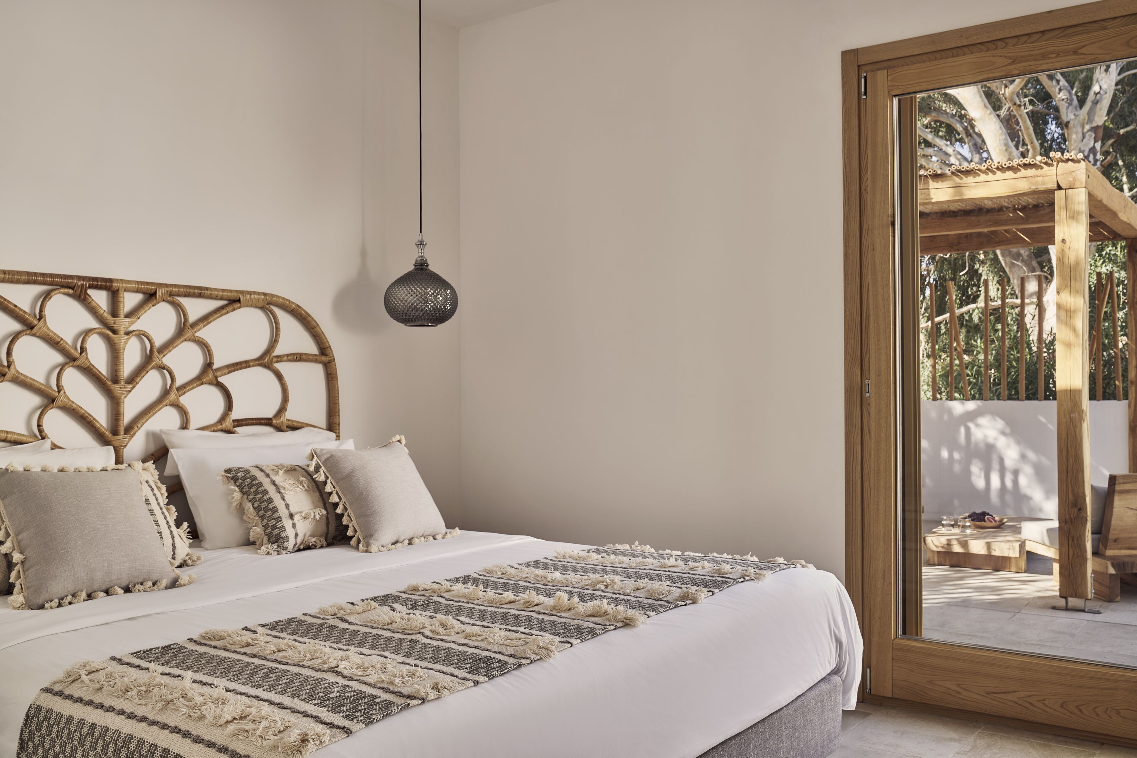 A bedroom with a large bed, a hanging lamp, and a view of an outdoor patio.
