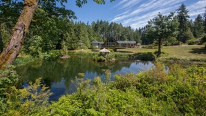 A lakeside cabin with a dock, surrounded by dense forest and a clear sky. - A Hidden Haven & Water Garden Cottages (Port Angeles)