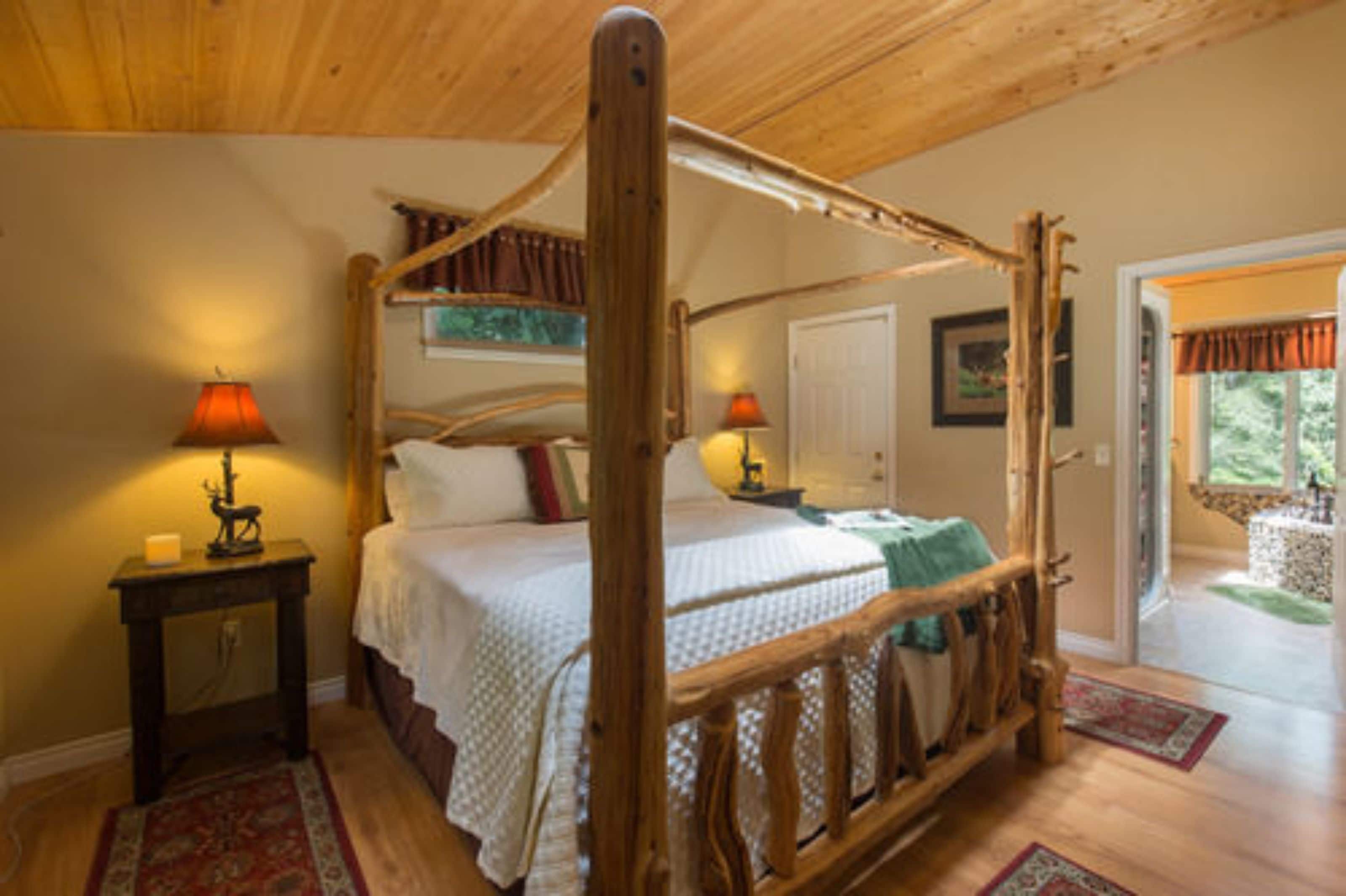 A four-poster bed with a wooden frame, a bedside table with a lamp, and a red rug on the floor.