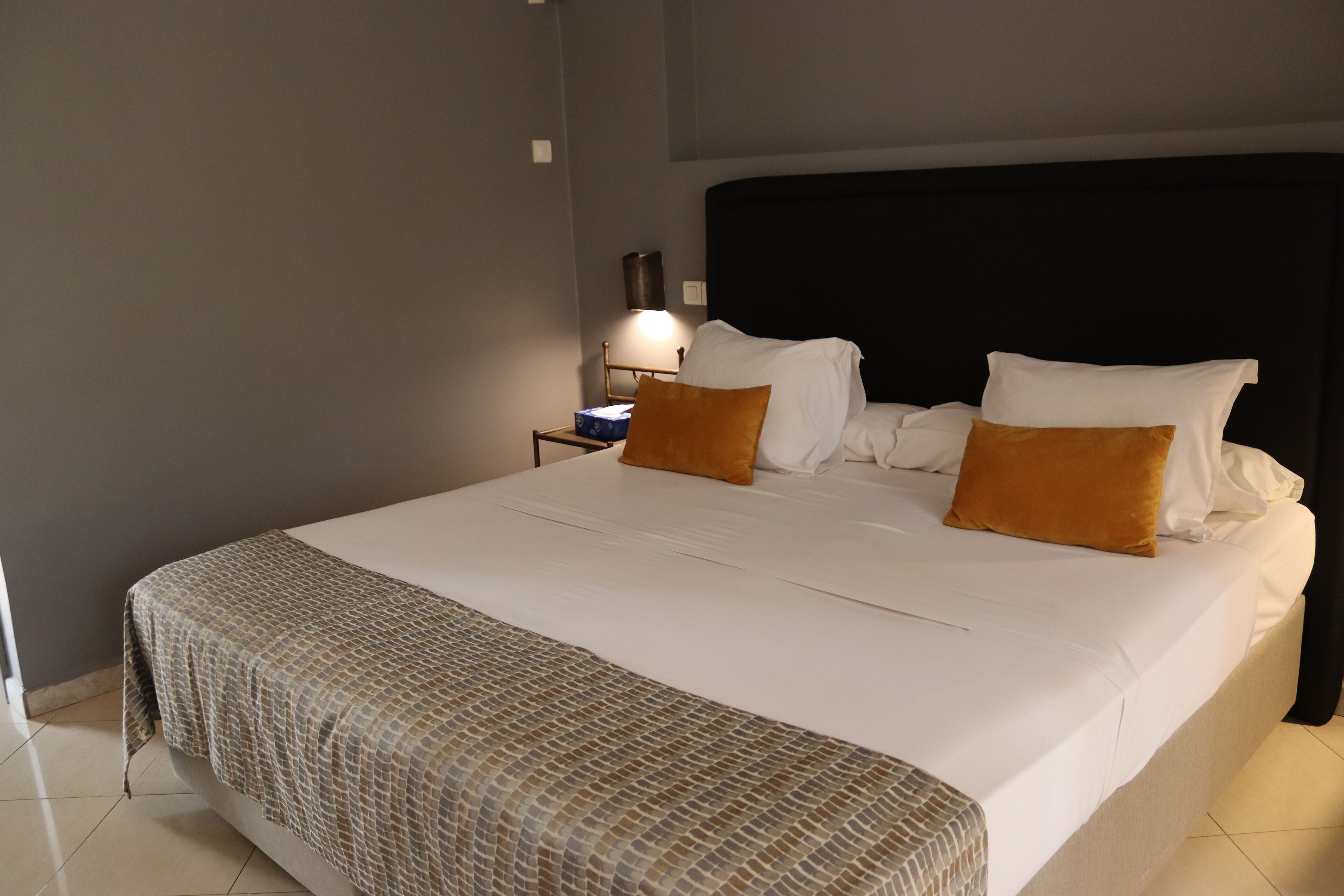A neatly made bed with white and orange pillows, a patterned bedspread, and a black headboard.