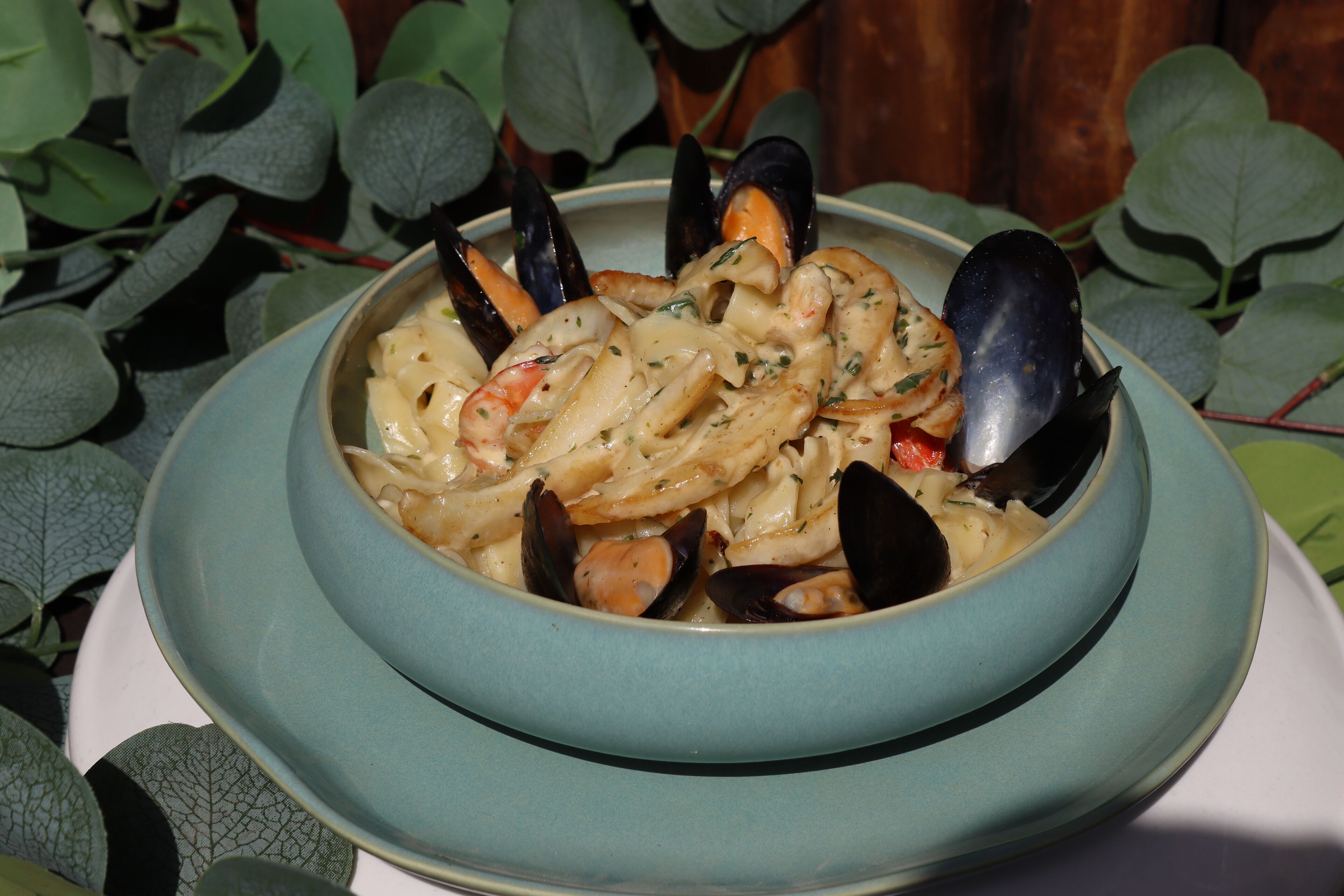 A bowl of seafood pasta with mussels and shrimp, surrounded by green leaves.