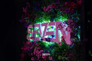 Un letrero decorativo con la palabra "SEVEN" rodeada de follaje y flores exuberantes.