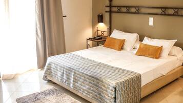 Quarto com cama, mesa de cabeceira, abajur e janela com cortinas.