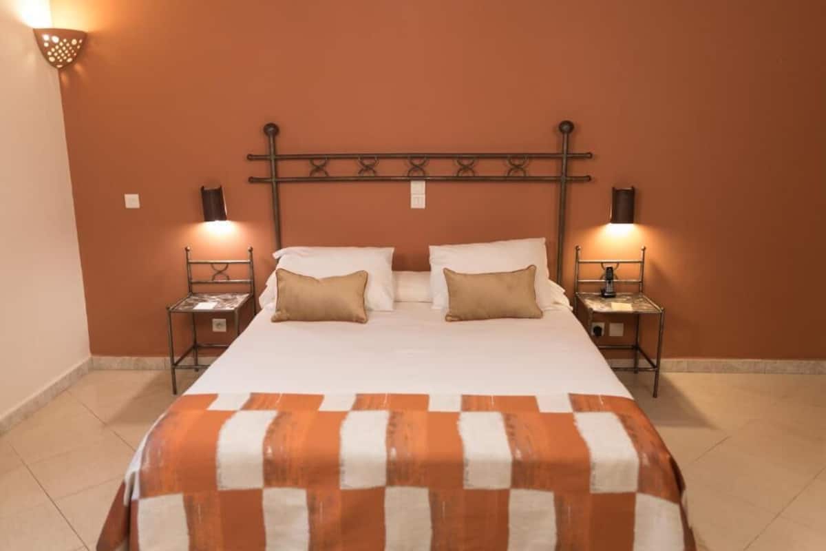 Un lit recouvert d’une couvre-lit à carreaux, deux tables de chevet avec des lampes et une croix accrochée au mur.