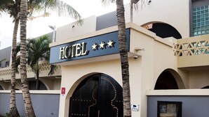 Entrada de hotel con un letrero, un arco grande y palmeras.