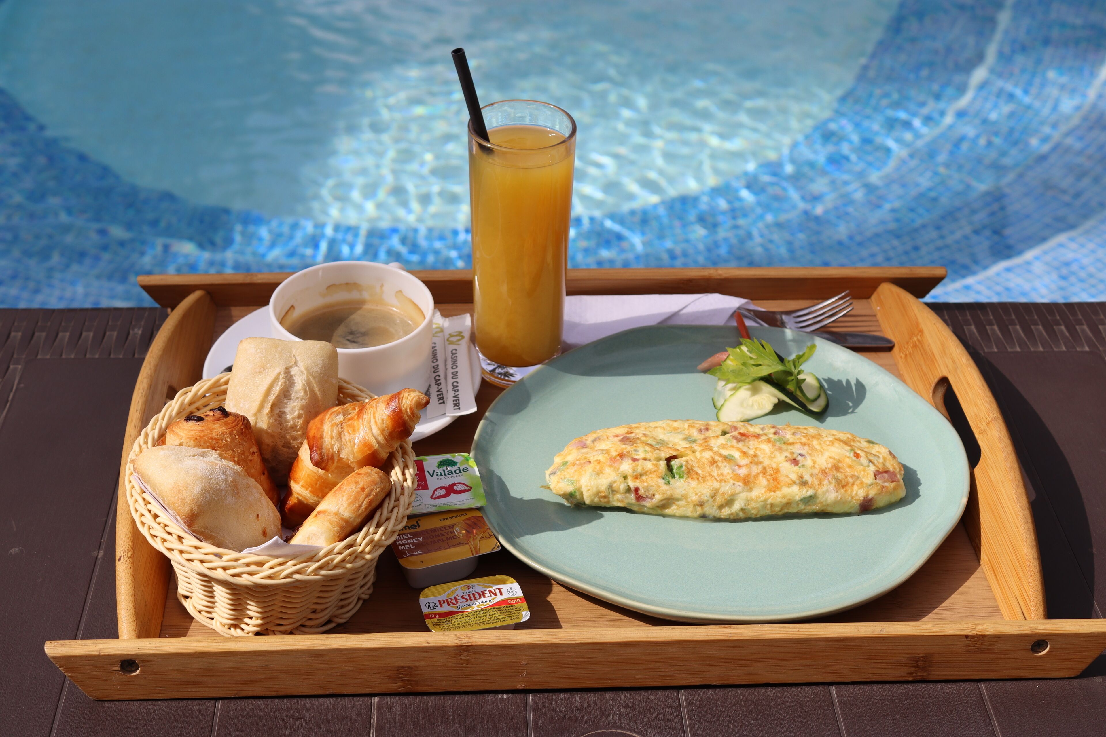 Un plateau contenant des viennoiseries, notamment des croissants, une assiette avec une omelette, un verre de jus d’orange et une tasse de café.