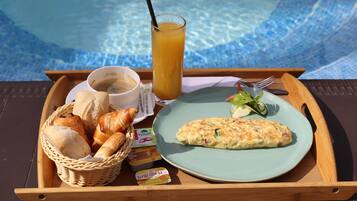 Un plateau contenant des viennoiseries, notamment des croissants, une assiette avec une omelette, un verre de jus d’orange et une tasse de café.