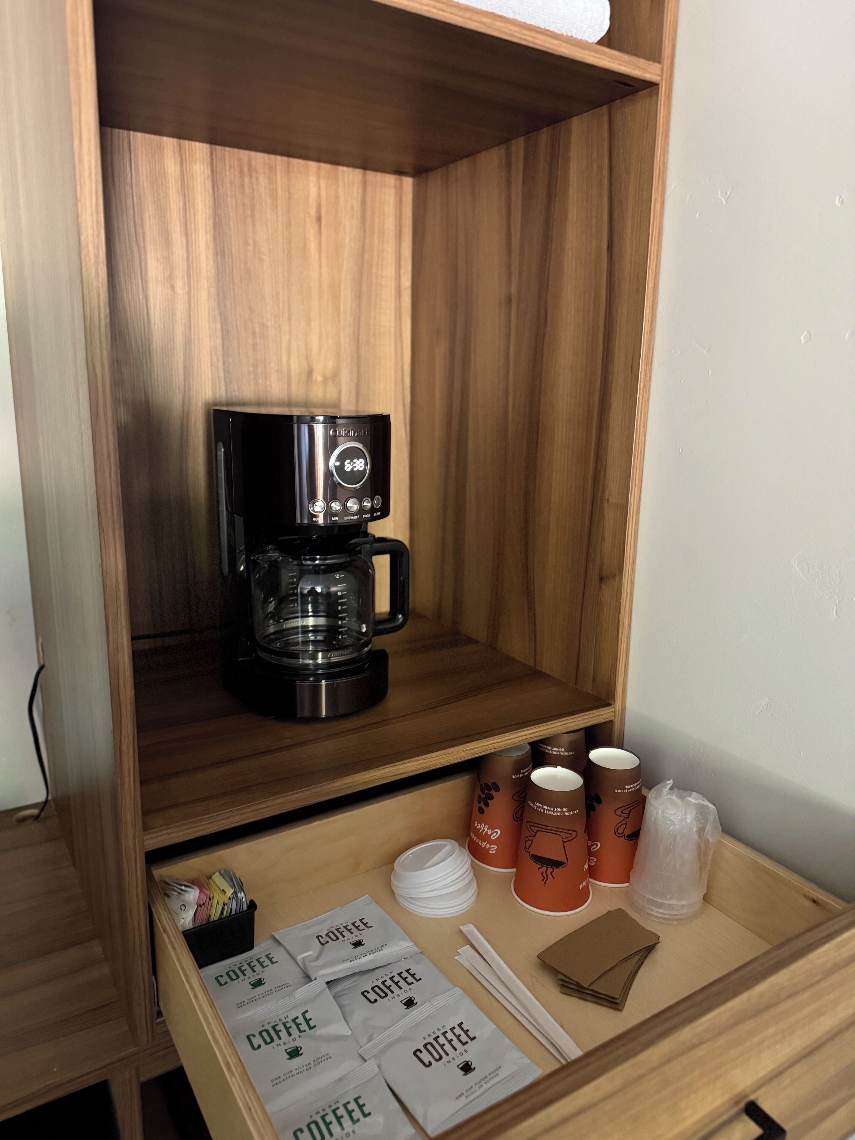 A wooden shelf with a coffee maker, disposable cups, and coffee packets.