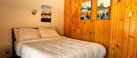 A single bed in a room with wooden panel walls, two paintings, and a ceiling light.