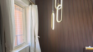 A room with a round wooden table, a brown chair, a hanging light fixture, and a window with curtains. - Lone Eagle Lodge (Grand Lake)