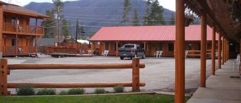 A rustic lodge with a red-roofed building, a covered outdoor seating area, and a view of a mountain range.