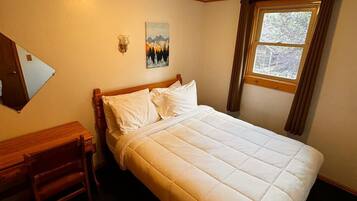 Un dormitorio con cama, escritorio, silla, un cuadro y una ventana.