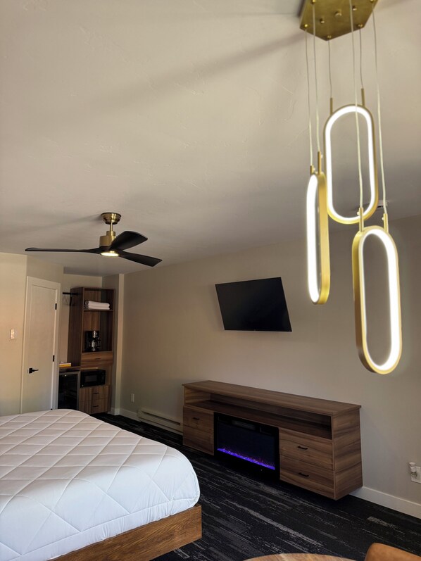 A bedroom with a bed, a ceiling fan, a TV, a wooden dresser, and a desk with a computer monitor. - Lone Eagle Lodge (Grand Lake)