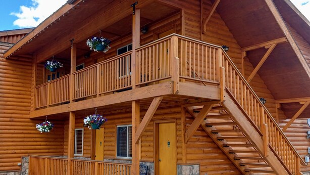 A log cabin with a two-story balcony, stone foundation, and a wooden staircase. - Lone Eagle Lodge (Grand Lake)