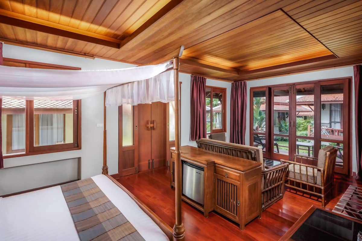 A room with a bed, wooden furniture, a small table, and large windows with curtains.
