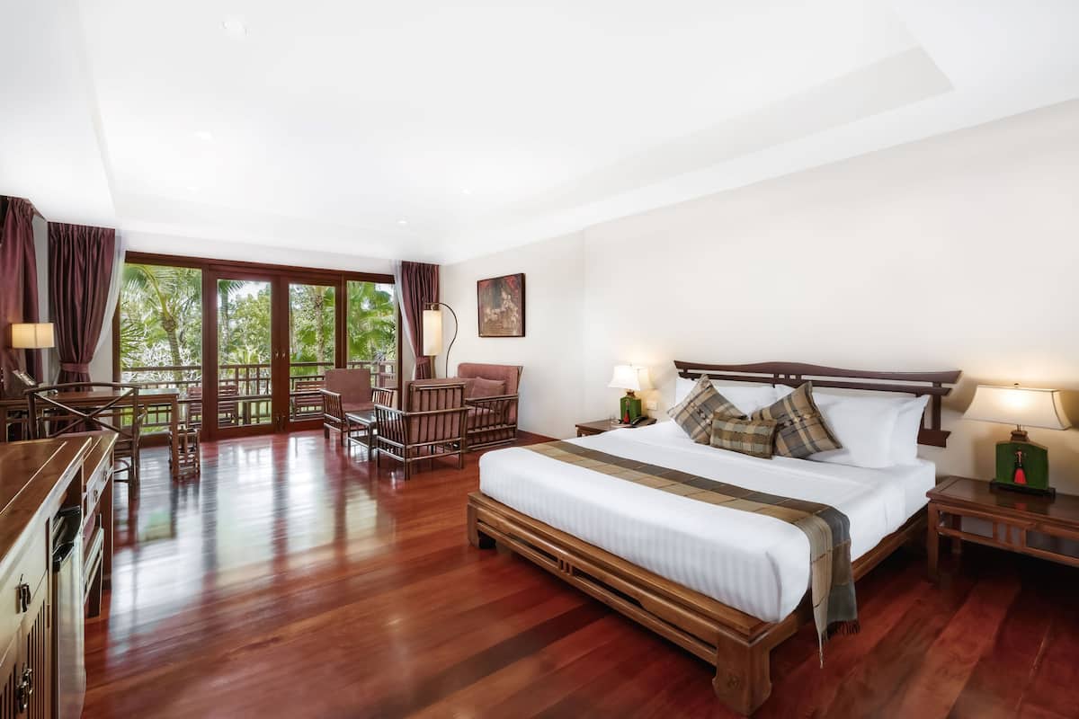 A spacious bedroom with a large bed, wooden headboard, and a view of the outdoors through large windows.