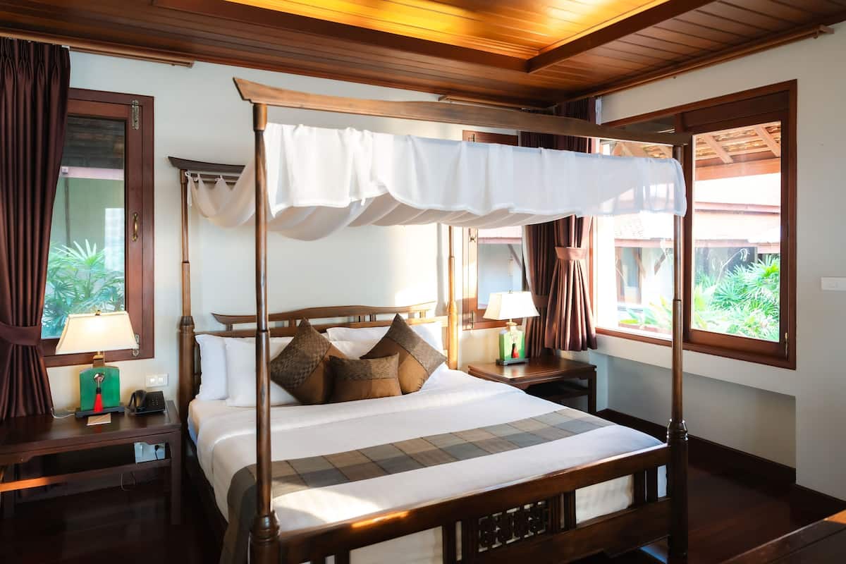 A four-poster bed with a canopy, a bedside table with a lamp, and a nightstand with a phone.