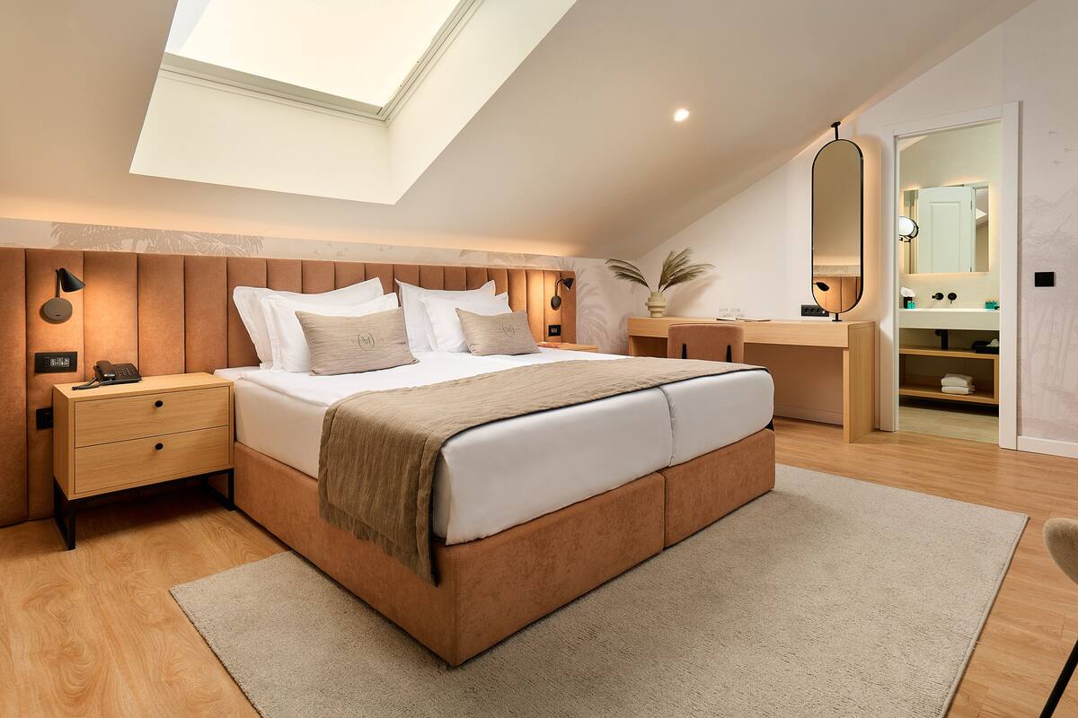 Un dormitorio moderno con tragaluces, una cama con cabecera de madera, una mesita de noche, un escritorio y un espejo.