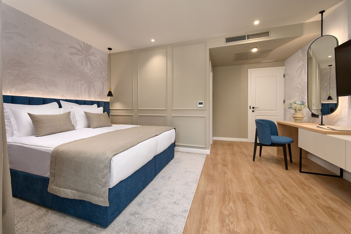 Un dormitorio con cama, escritorio, silla y un espejo grande.