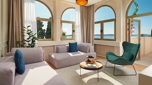 A modern living room with a sofa, armchair, and coffee table, large windows with arched tops, and a view of the sea.