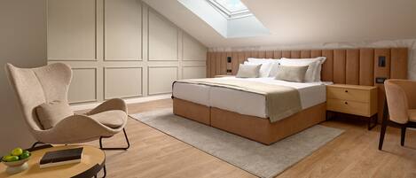 A bedroom with a skylight, a bed, a nightstand, a chair, and a small table with a bowl of fruit.