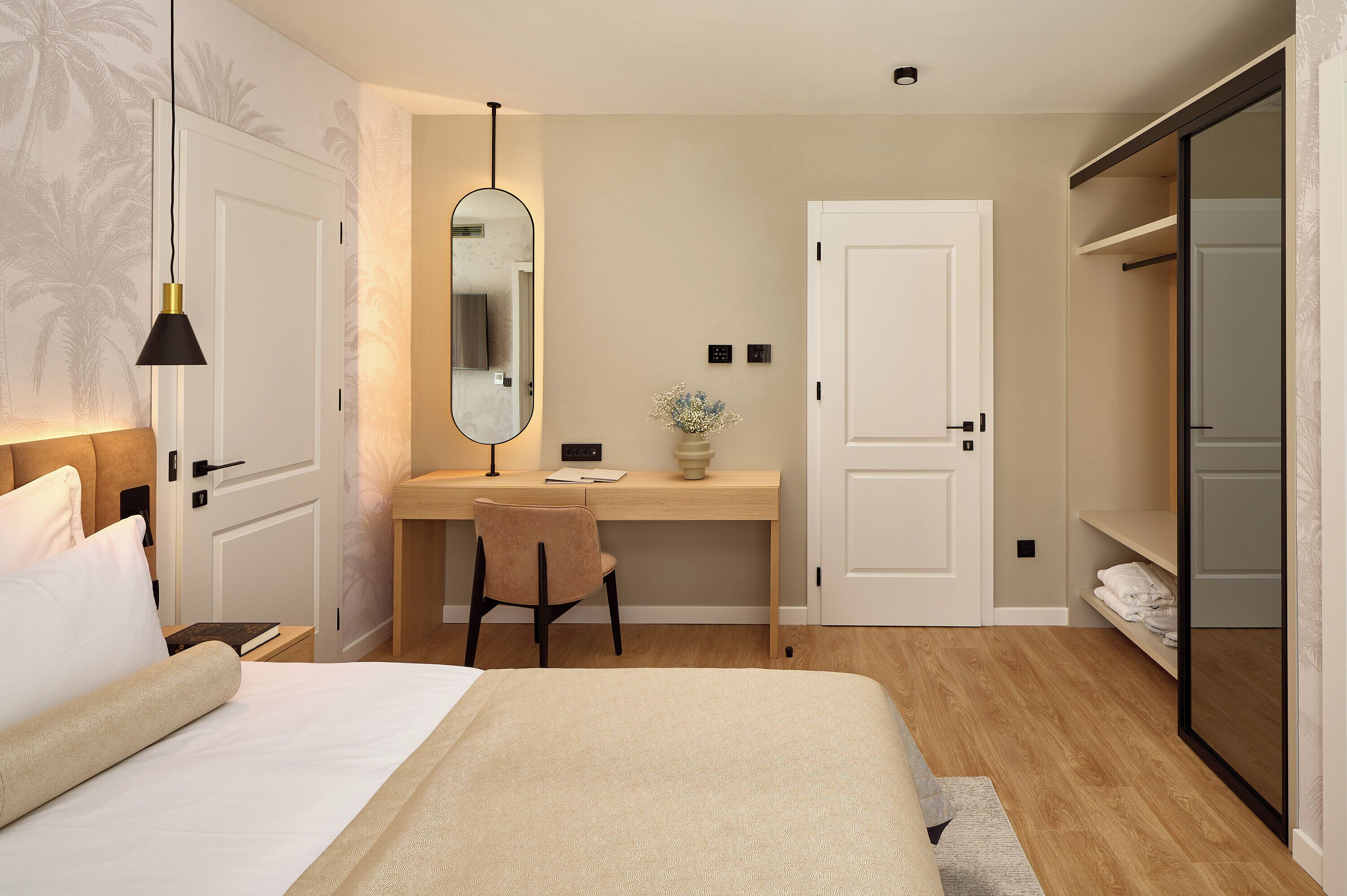 A bedroom with a bed, a desk, a chair, a mirror, and a wardrobe.