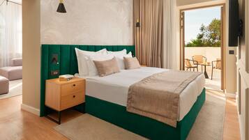 Een hotelkamer met een groen gestoffeerd hoofdeinde, een groot bed met witte lakens, een houten nachtkastje, een beige vloerkleed en uitzicht op het buitenterras.