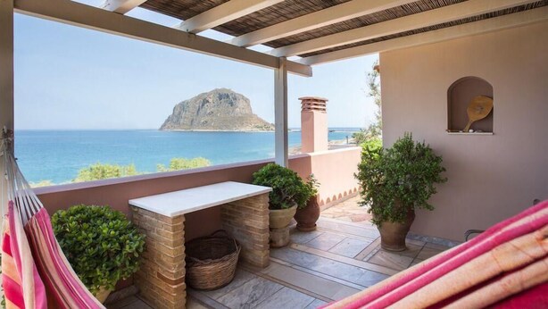 A balcony with a view of the sea, a hammock, a table, and potted plants.