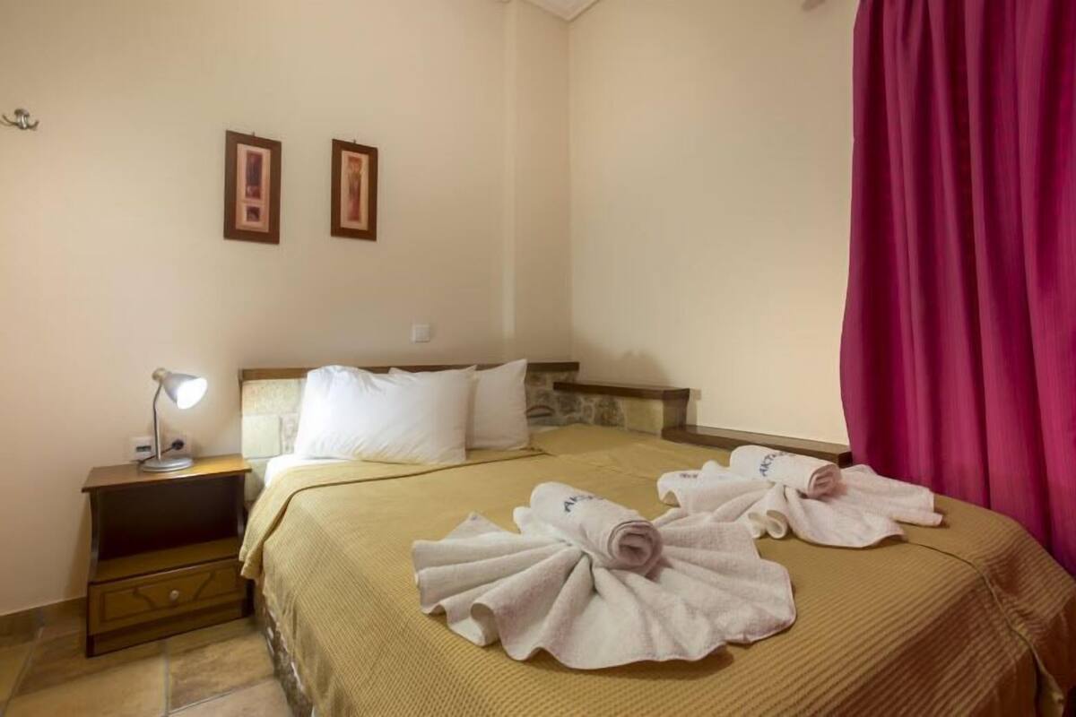 Una habitación de hotel con cama, almohadas, mesita de noche, lámpara y toallas.