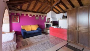 A room with a wooden ceiling, a blue sofa with yellow cushions, a red cabinet, and a television on a white shelf.