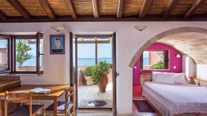 A room with a bed, a desk, and a view of the sea through an open door.