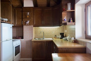 A kitchen with wooden cabinets, a white stove, a sink, and a window. - Aktaion Hotel (Monemvasia)