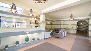 A hotel lobby with a reception desk, seating area, and decorative plants. - Hotel Villamare (Syracuse)