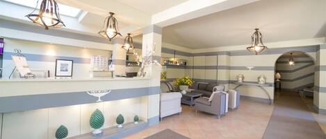 A hotel lobby with a reception desk, seating area, and decorative plants.