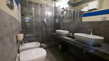 Een moderne badkamer met een douchecabine van glas, twee wastafels en een toilet.