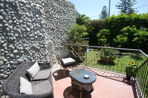 Un balcón con mobiliario de mimbre, un muro de piedra y vistas a un jardín.