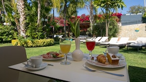 A table set with a plate of food, a glass of orange juice, a glass of red drink, a white vase, and a cup. - Hotel Villamare (Syracuse)