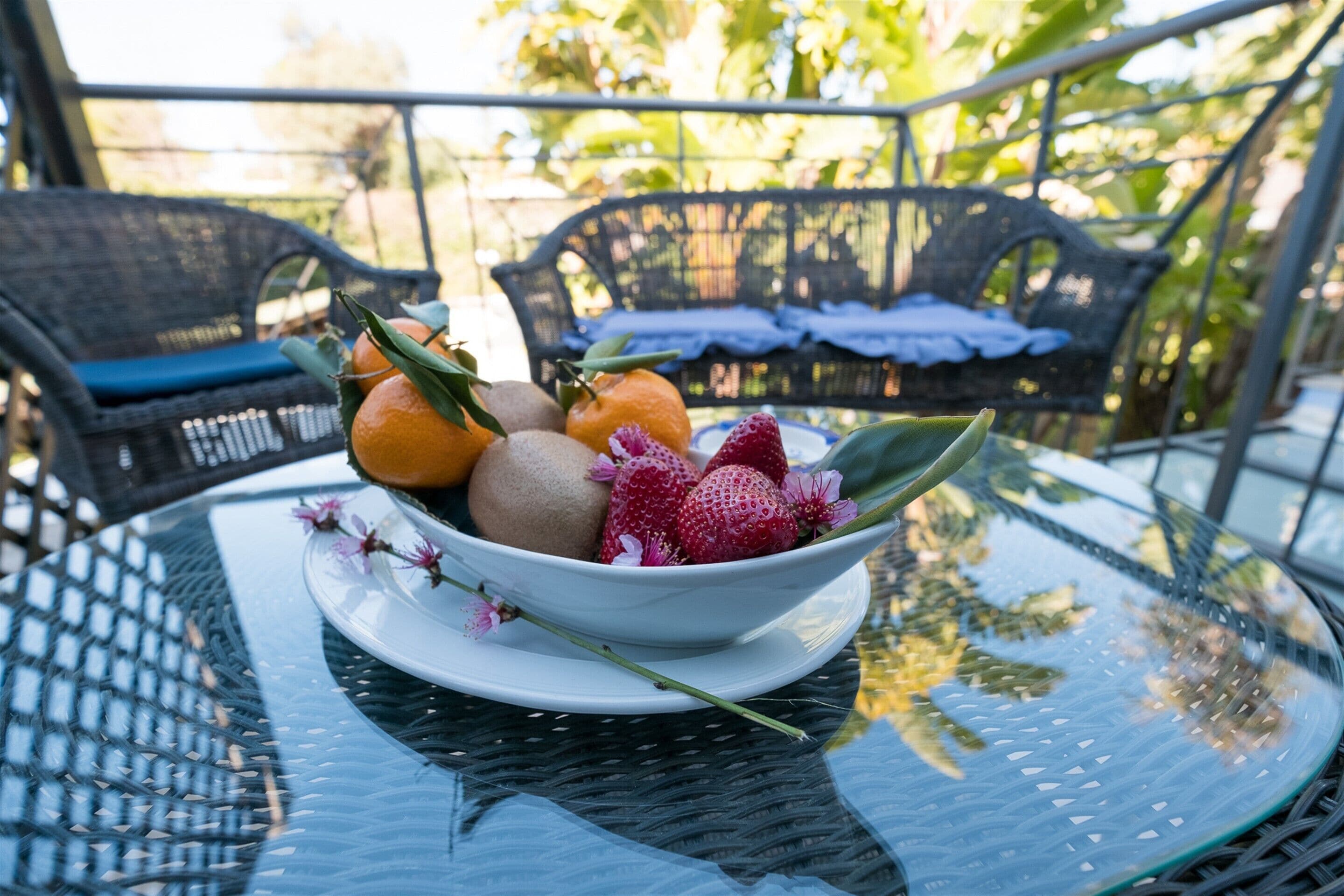 A glass table with a bowl of fruit and flowers.
