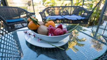 A glass table with a bowl of fruit and flowers.
