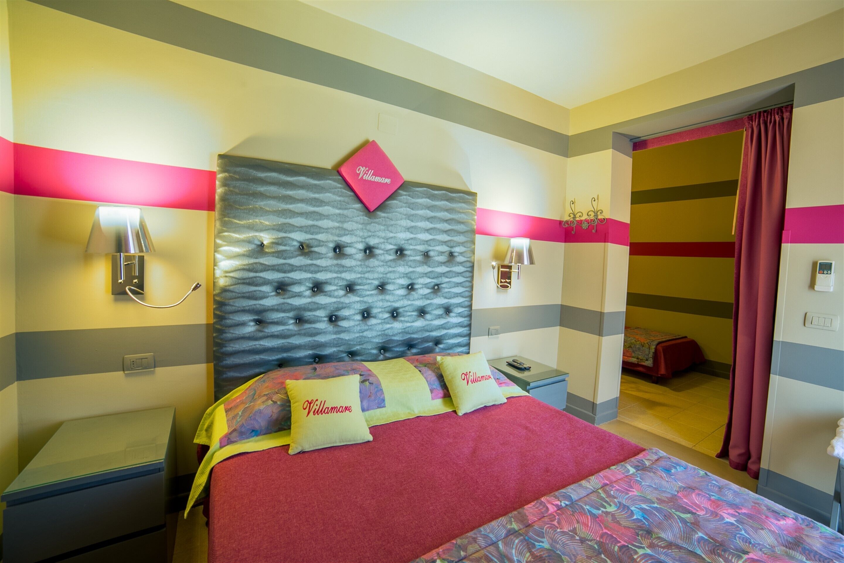 Una camera d'albergo con un letto, due comodini, una testiera e una porta che dà su un'altra stanza.