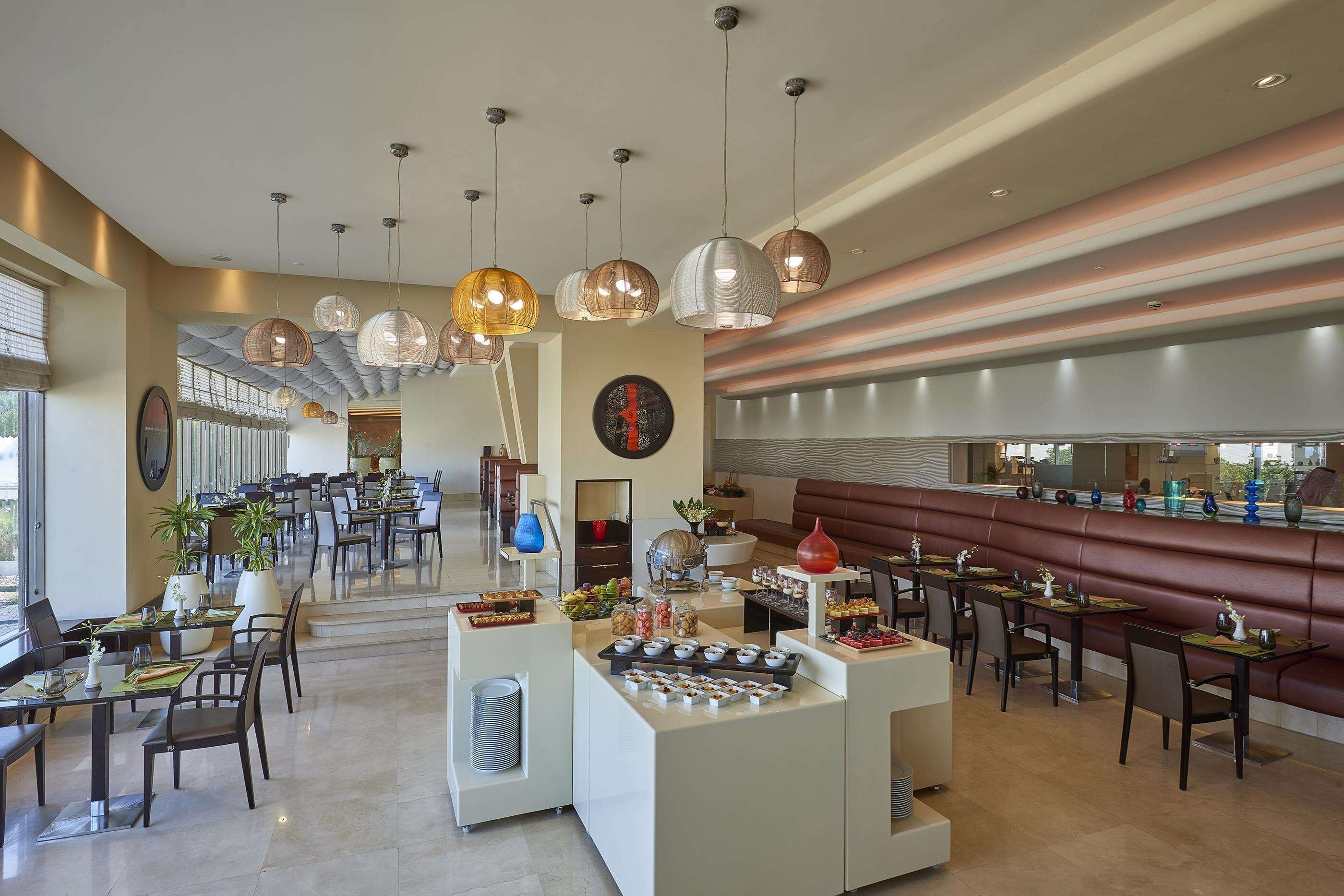 A modern restaurant with a long counter, multiple seating areas, and decorative hanging lights.
