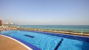 A swimming pool with a view of the ocean, lounge chairs, and a covered area. - Safir Fintas Kuwait Hotel (Fintas)