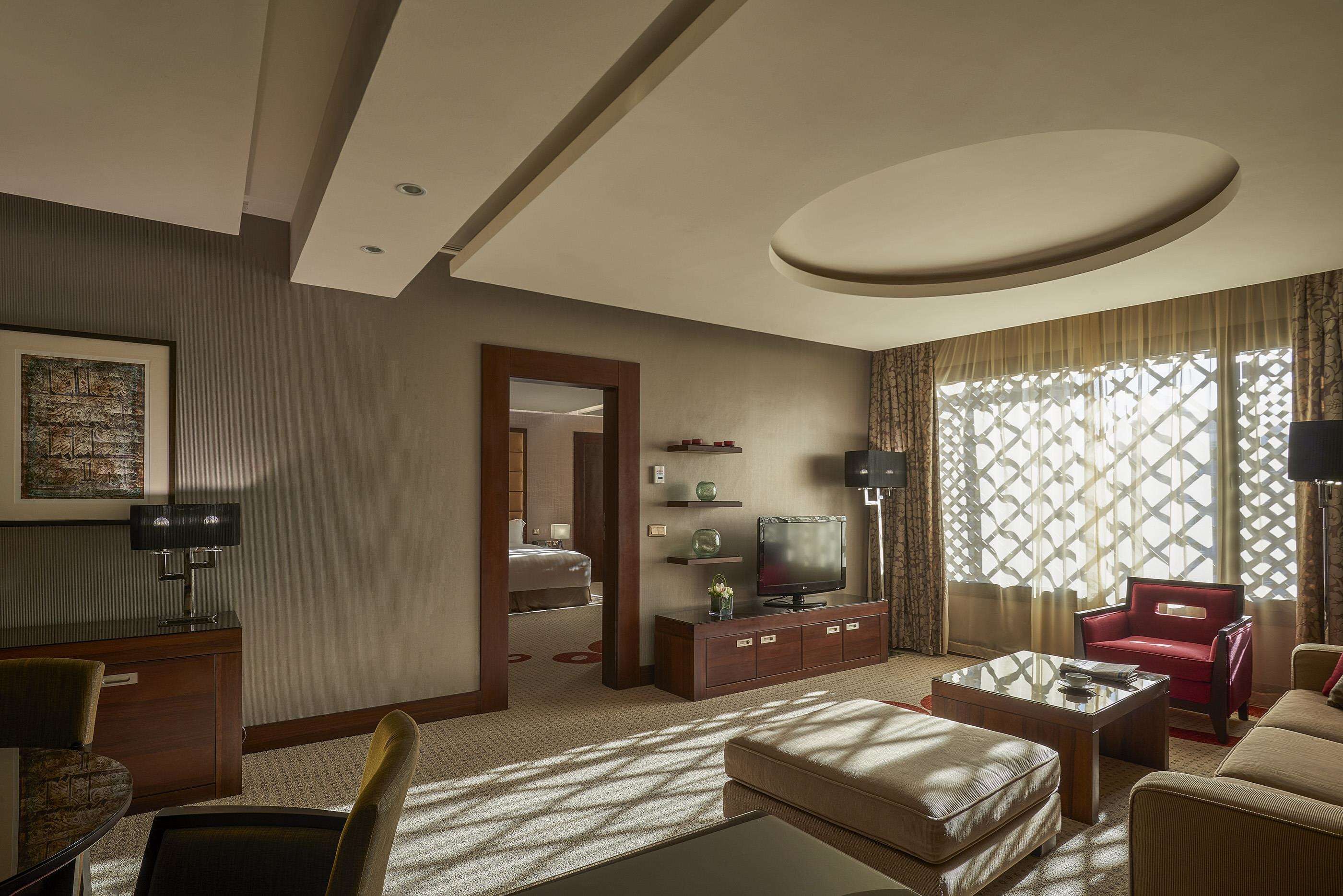 Una habitación de hotel con una cama grande, un televisor sobre un mueble de madera, un sillón rojo, un sofá beige y una mesa de centro.