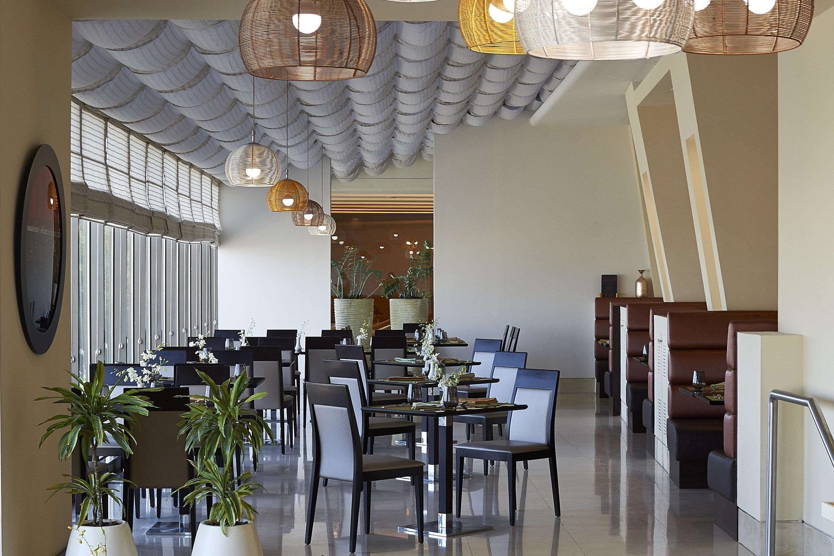 Un restaurante moderno con techos altos, lámparas de mimbre colgantes y una zona central de comedor con mesas y sillas.