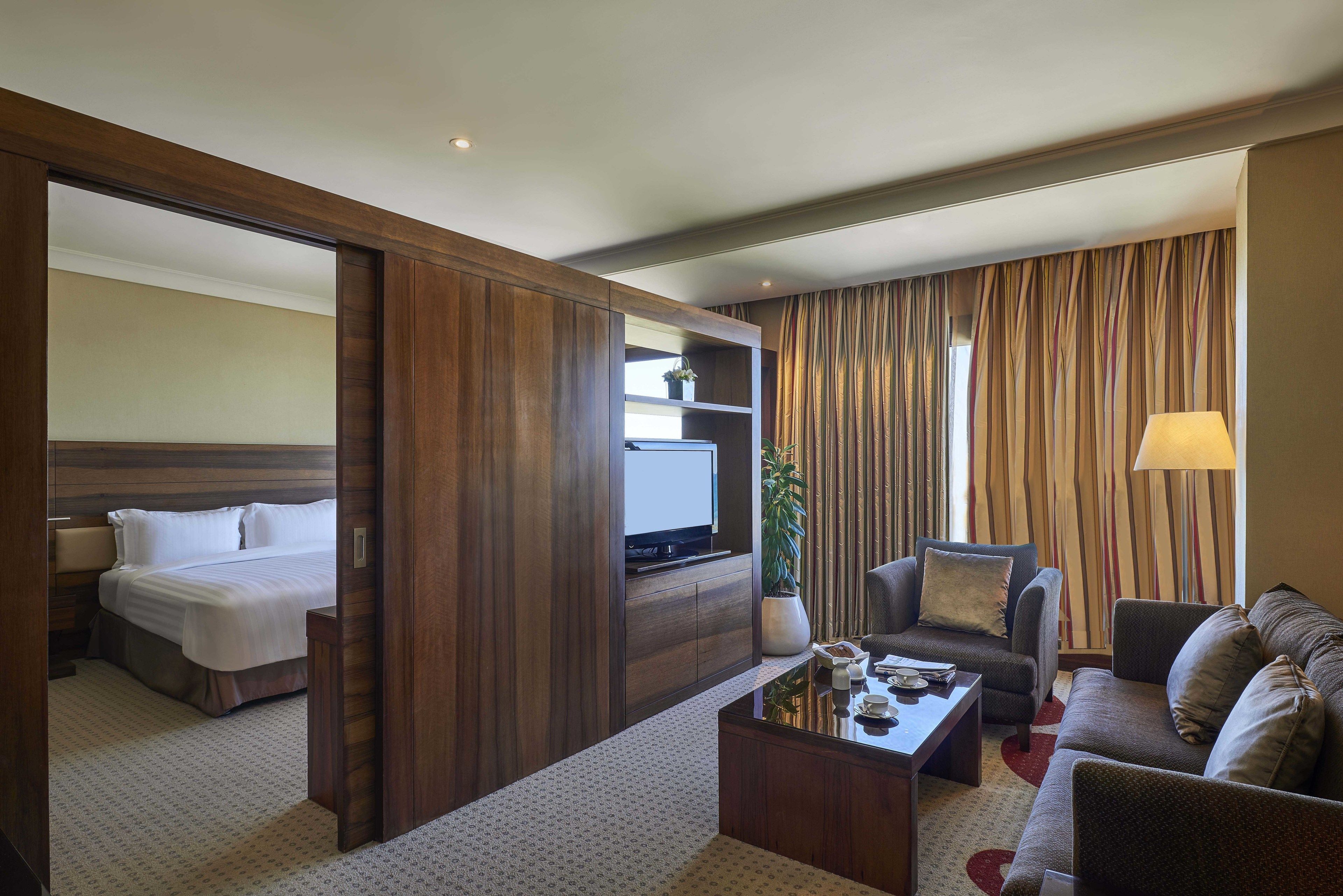 A hotel room with a bed, a TV, a sofa, a coffee table, and a plant.