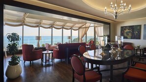 A spacious dining area with a large round table, red upholstered chairs, and a view of the ocean through large windows. - Safir Fintas Kuwait Hotel (Fintas)