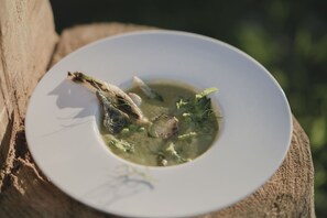 A white bowl of soup with a piece of meat and vegetables on a wooden surface. - Agriturismo I Pini (San Gimignano)