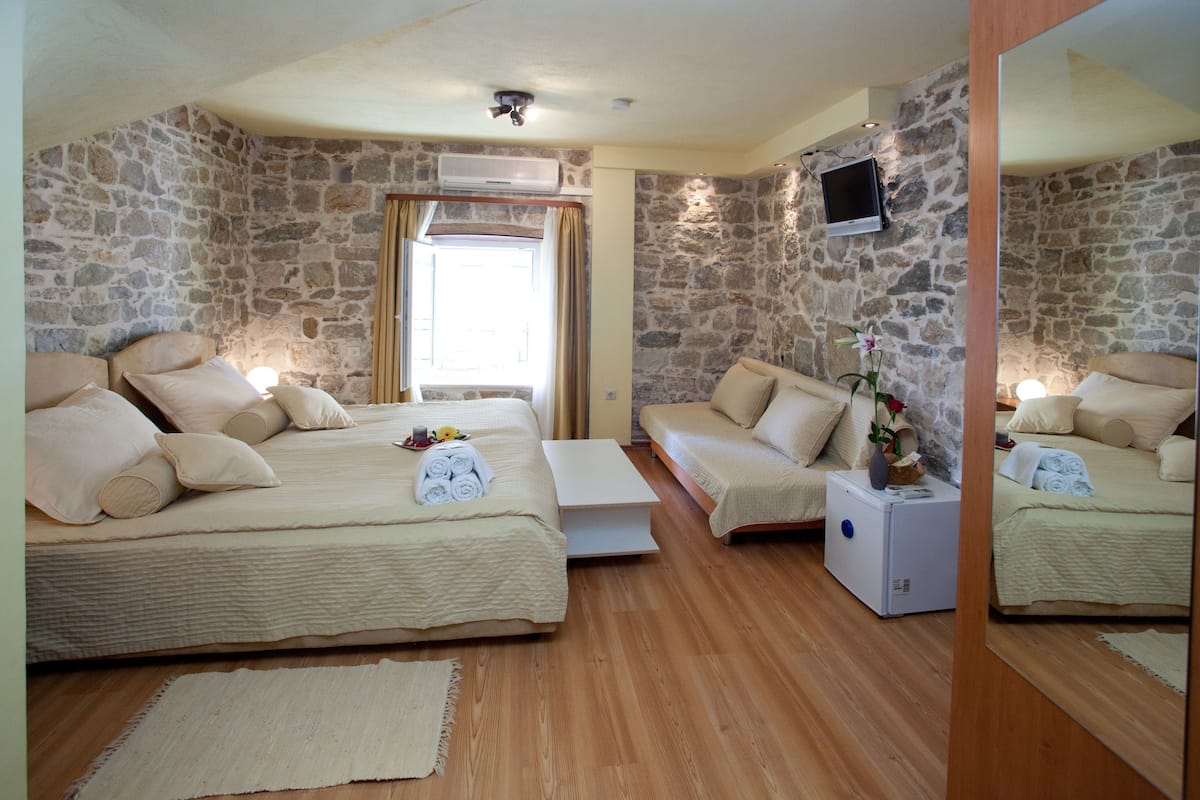 A bedroom with a stone wall, a bed, a sofa, a small table, and a TV mounted on the wall.